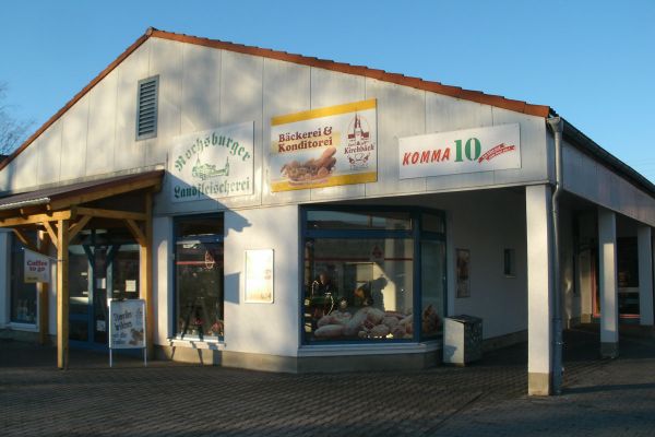 Zum Kirchbäck – Filiale Penig Frontansicht Haus mit verschiedenen Geschäften, daran Schild mit Aufschrift „Bäckerei und Konditorei Zum Kirchbäck“