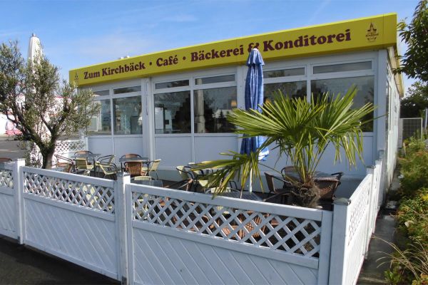 Filiale Hartmannsdorf (Kress-Parkplatz) weißer Flachbau mit Außensitzbereich, am Haus Schriftzug „Zum Kirchbäck: Café, Bäckerei & Konditorei“