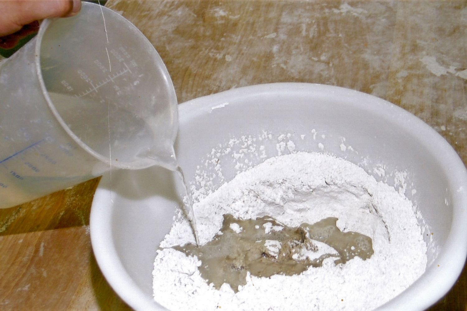 Zum kleinen Stück Natursauerteig vom Vorabend geben wir Roggenmehl und Wasser. In einer Schüssel wird der Natursauerteig mit Roggenmehl und Wasser gemischt.